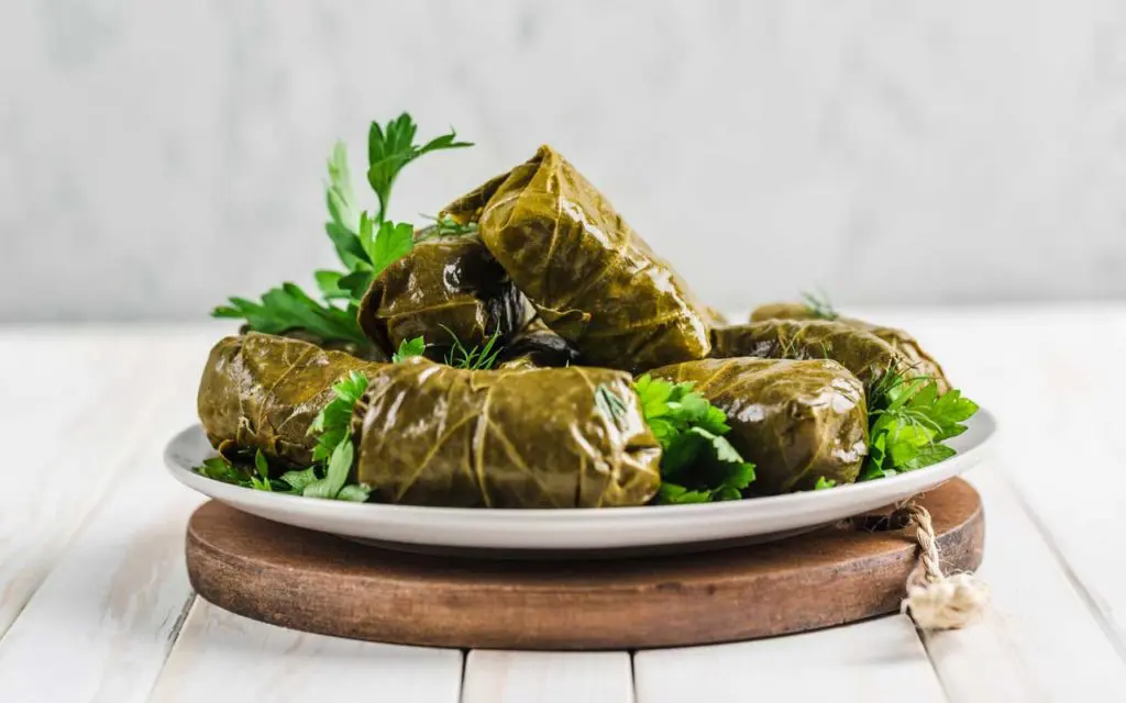 Mediterranean food: dolmas (delicious stuffed grape leaves on a plate with fresh cilantro on a wooden background)