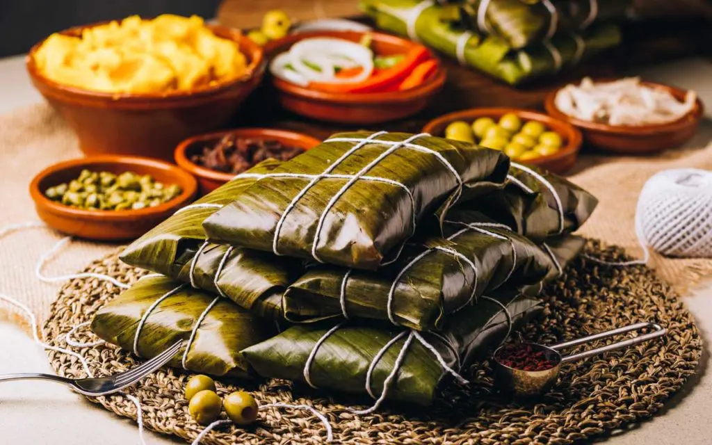Venezuelan Food: Hallacas (Meat Tamales) stacked on a table, served with various sides.