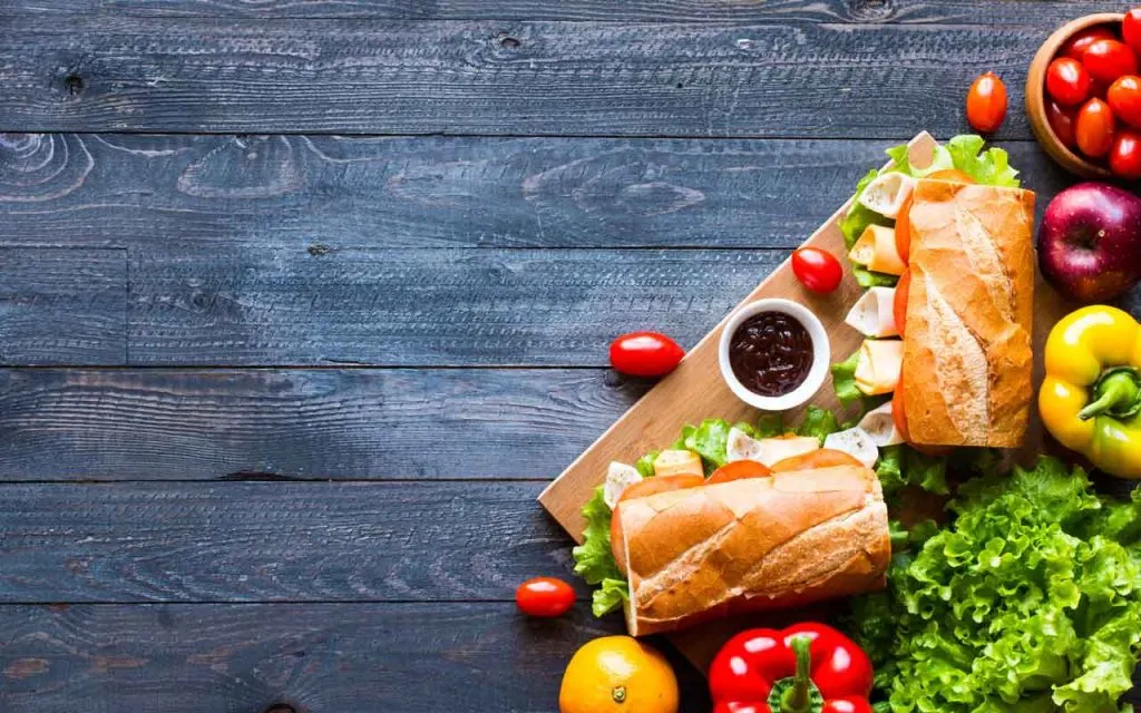 Sandwiches with turkey or chicken on a wooden board served with tomatoes, lettuce, and peppers.
