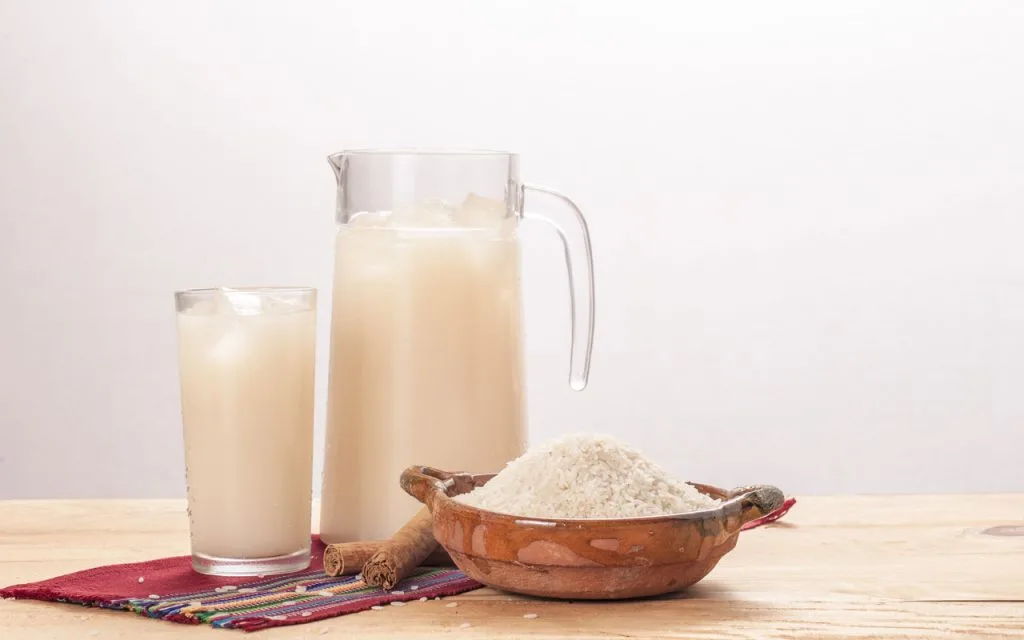 Horchata, a sweet rice and seed beverage in a glass pitcher and a glass with ice.