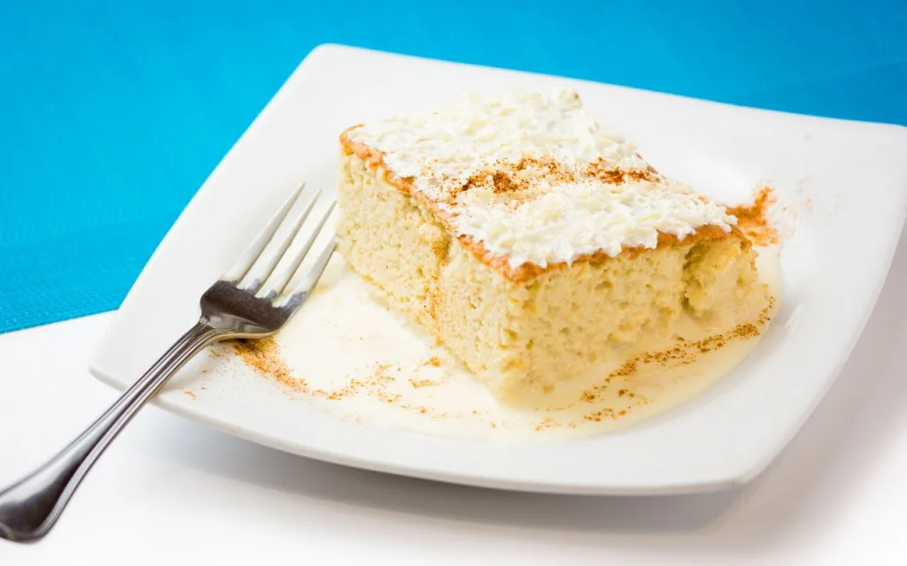 A slice of tres leches cake on a white plate on the table.