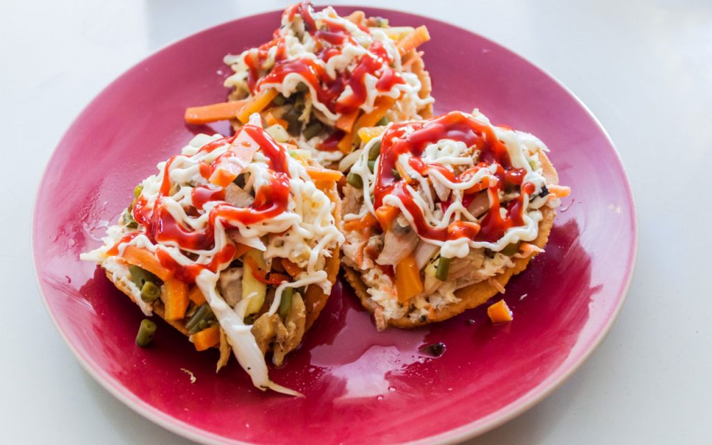 Salvadoran enchiladas – 3 fried tortillas with toppings on a plate.
