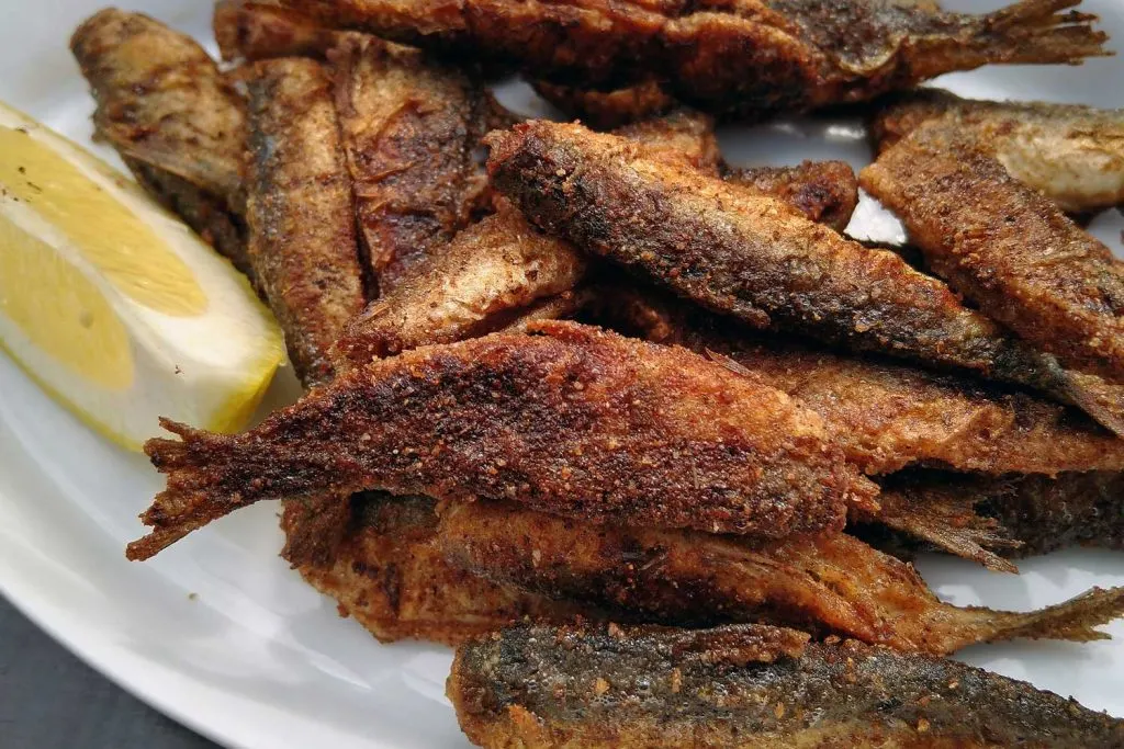 Multiple Paistetut Muikut (Fried Vendace) on a white plate with a lemon slice.