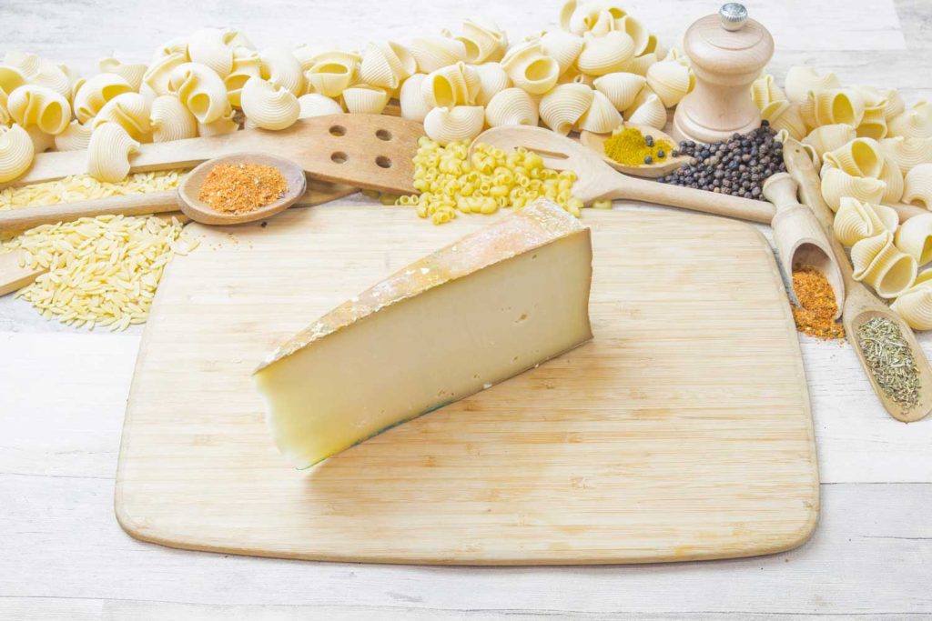 Fontina cheese on a wooden board with raw past and spices around it