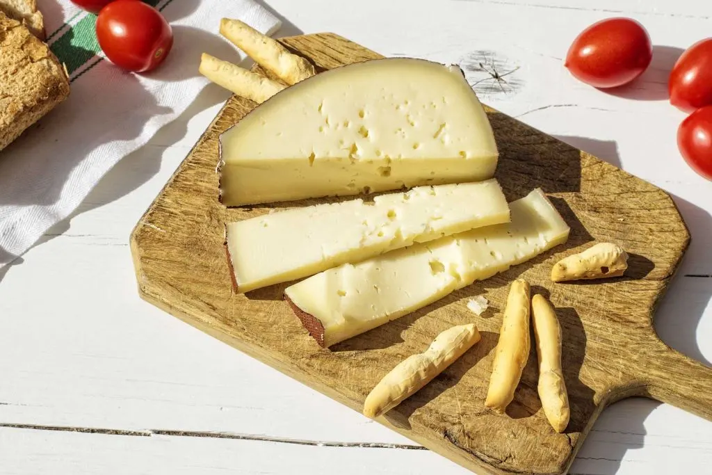 Asiago cheese slices and bread sticks on a wooden board with cherry tomatoes on the table