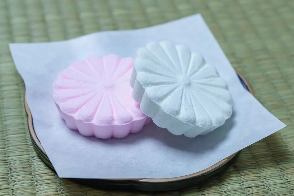 Two Rakugan (Dried Japanese Sugar Candies) - one blue and one pink on a small plate.