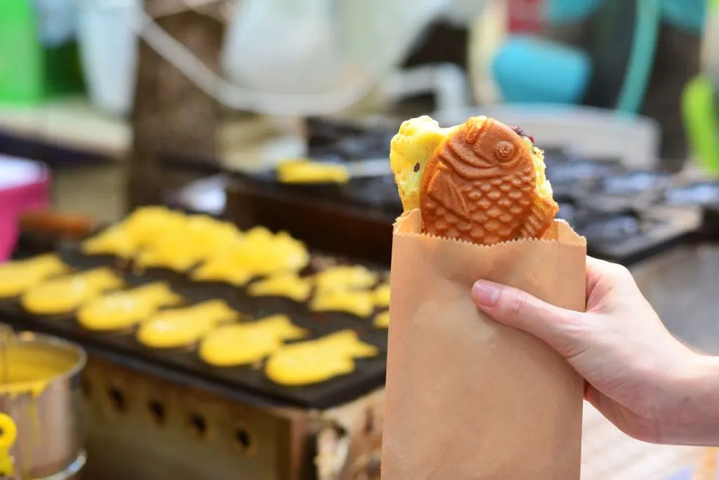 Holding the Japanese dessert Taiyaki (a fish-shaped cake with fillings) in a street food market.