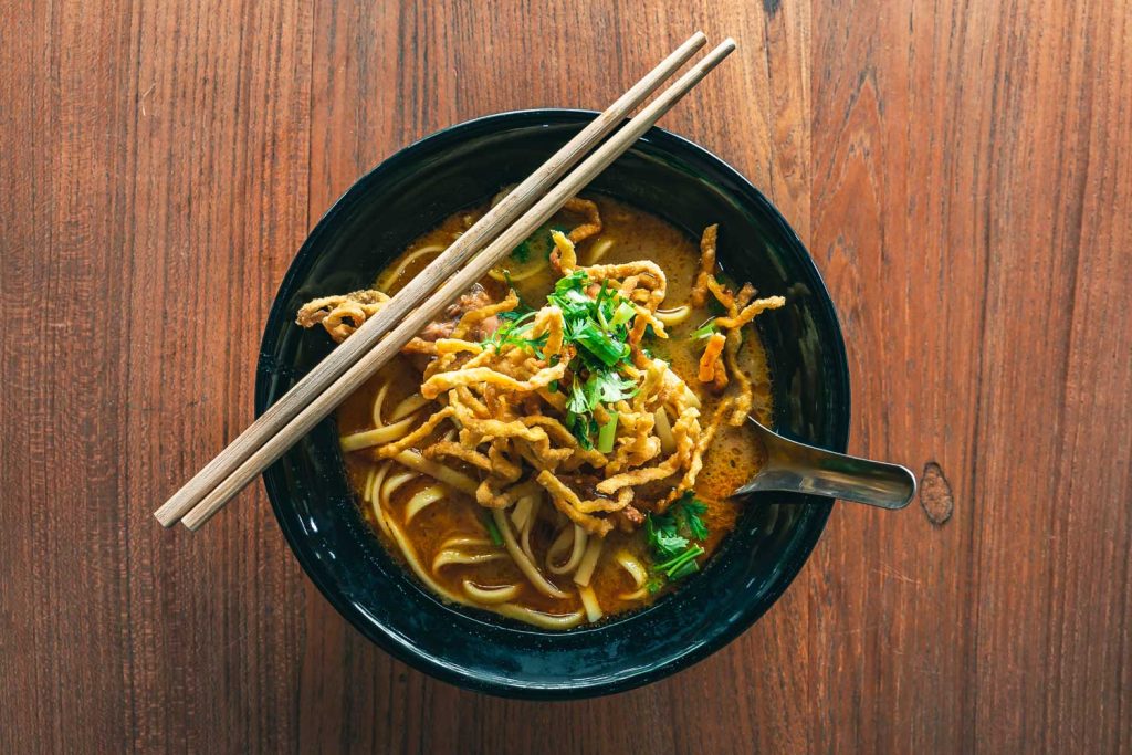 Northern Thai Style Egg Noodles in a deep bowl with a spoon and chopsticks.