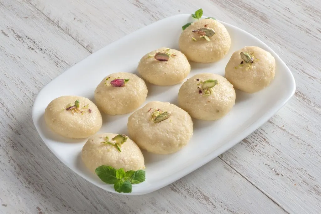 Milk peda, an Indian sweet resembling fudge, topped with pistachios, served on a plate.