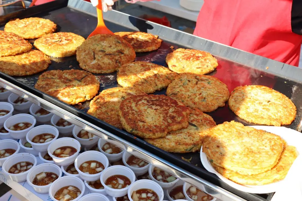 Bindaetteok or mung bean pancakes being prepared at a street food vendor's stall.
