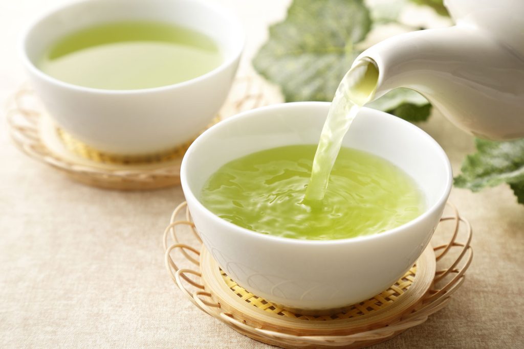 Green tea being poured in white cups.