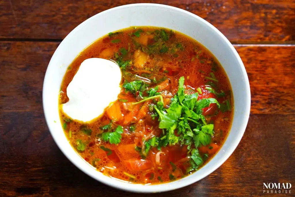 Borscht in a bowl, topped with a dollop of sour cream and parsley. Moldovan Food - Bors | Borscht
