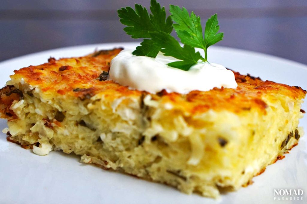 Patatnik on a plate, topped with sour cream and parsley.