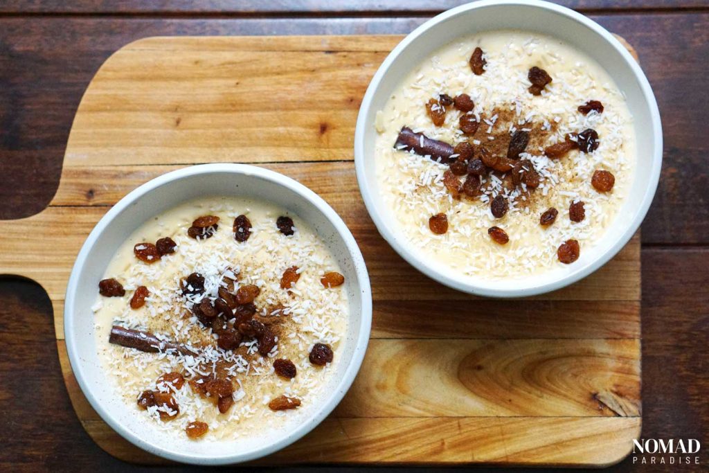 Arroz con leche in bowls with ground cinnamon, shredded coconut, and raisins on top.