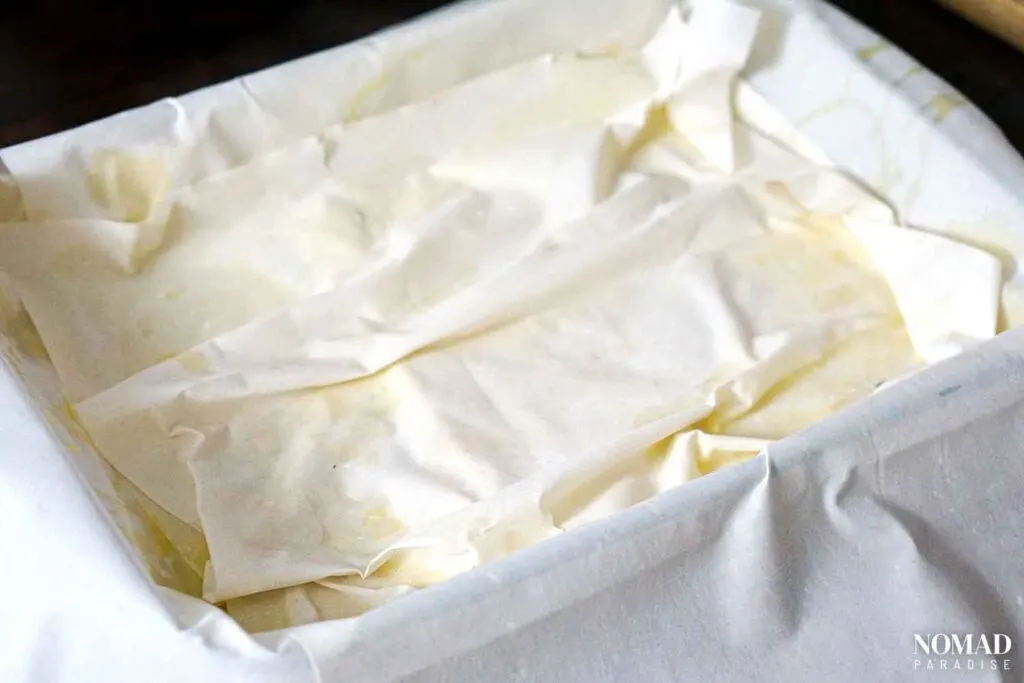 Spanakopita recipe step-by-step (layering the filo dough and brushing with olive oil).