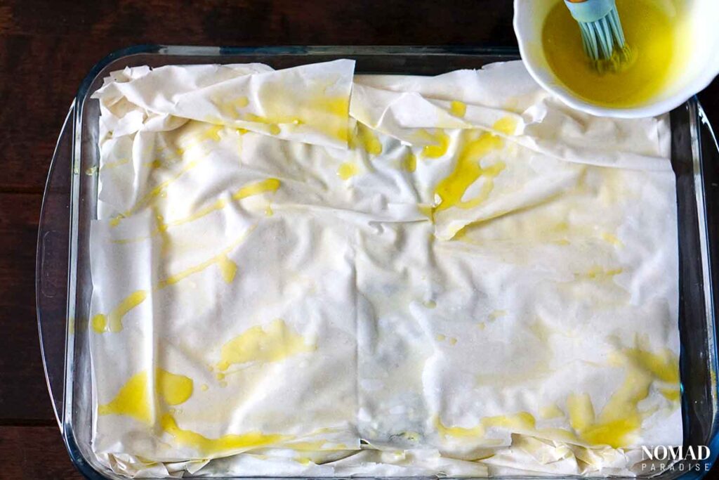 Spanakopita recipe step-by-step (adding the top filo dough layers and brushing with olive oil).