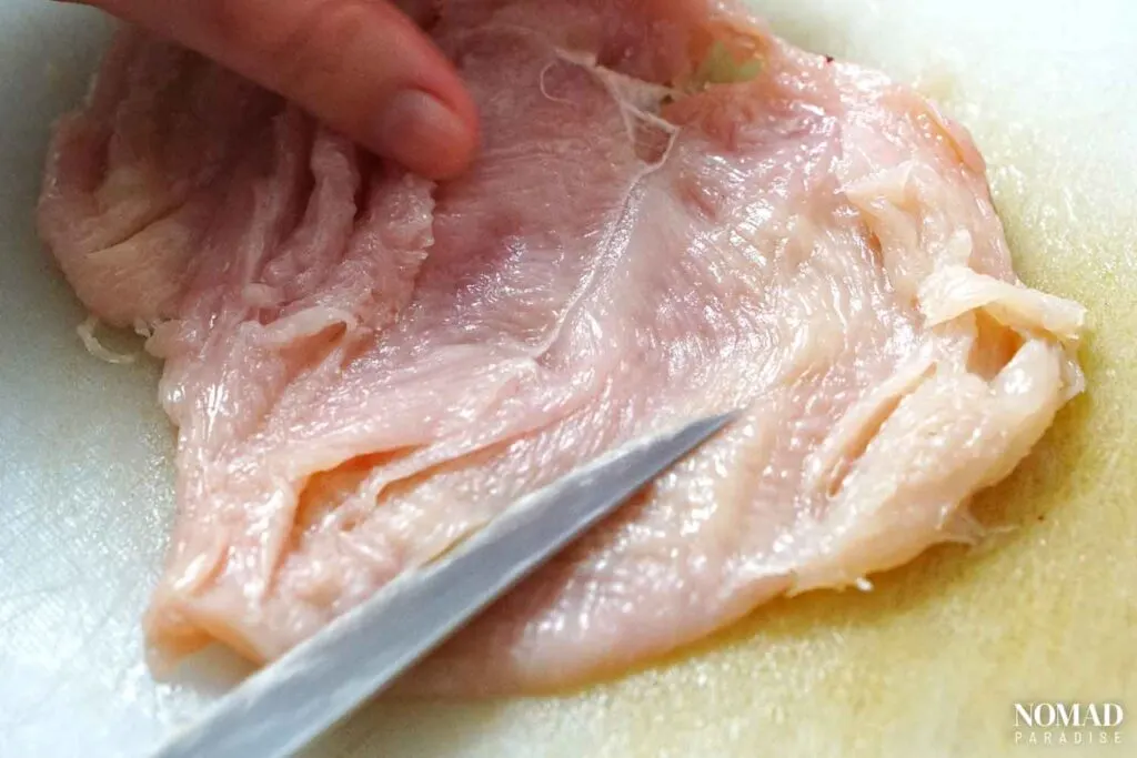 Flattening the chicken breast by doing little cuts with a knife.