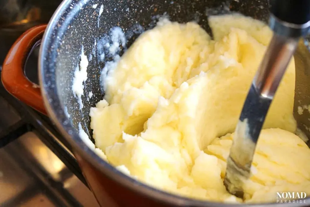Adding melted butter and warm milk to mashed potatoes.